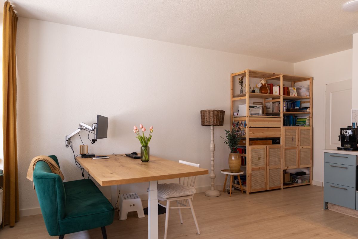 Een ruimte met een grote tafel die in hoogte verstelbaar is, een groen zitbankje en een witte stoel. Op de achtergrond zie je een houten boekenkast.